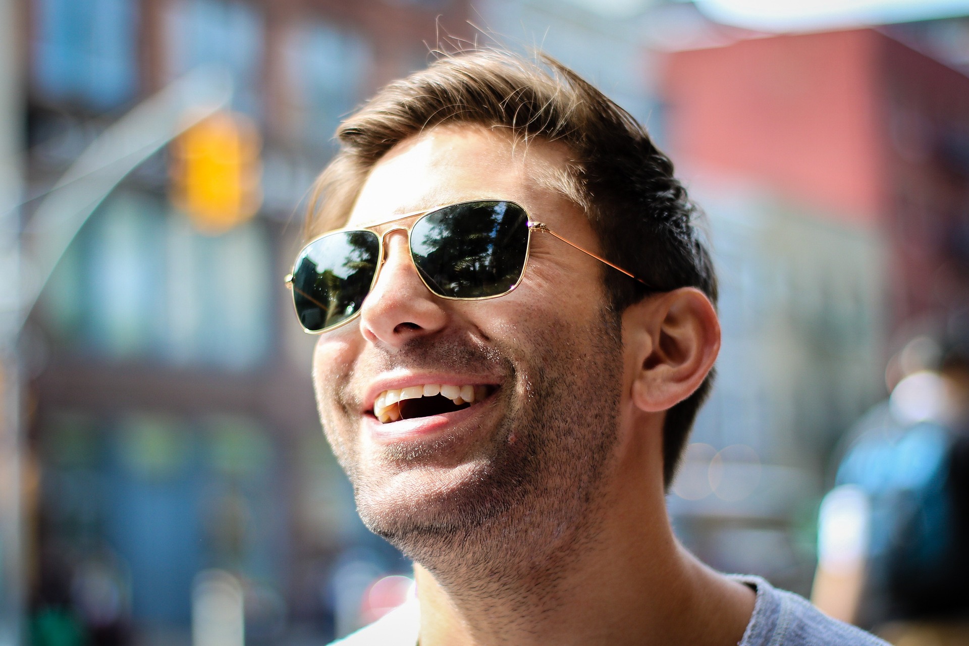 Portrait of man in white shirt and sunglasses smiling in the city, close up